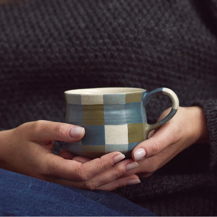 Person holding a checkered mug with a dark textured sweater background