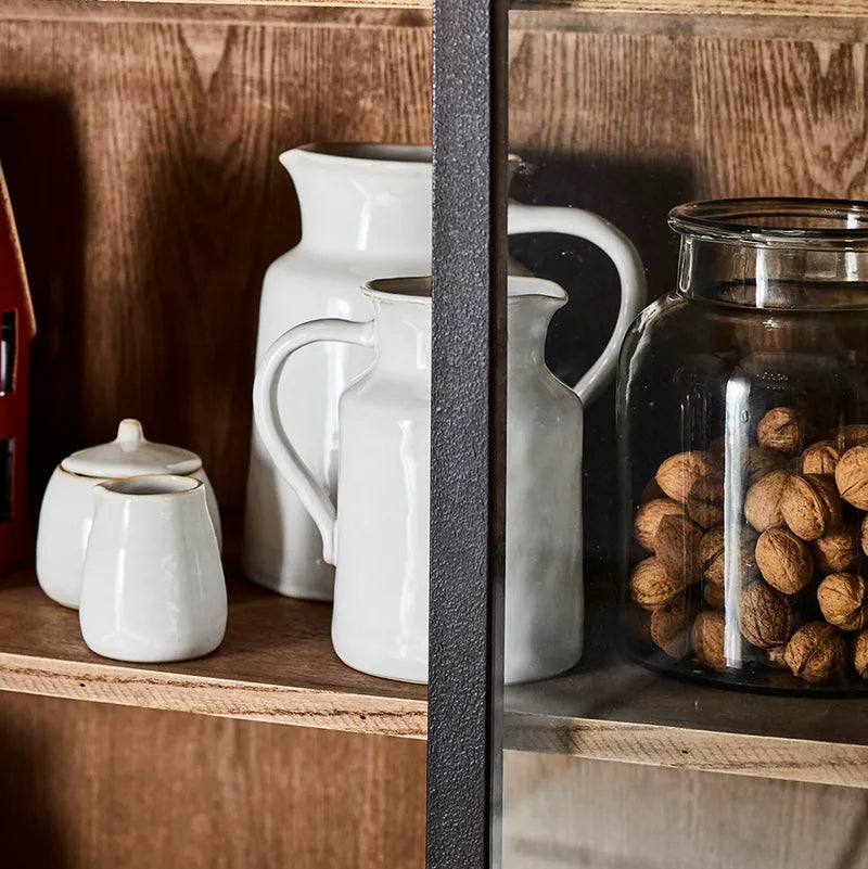 Wooden shelf with ceramic pitchers and a glass jar filled with nuts.
