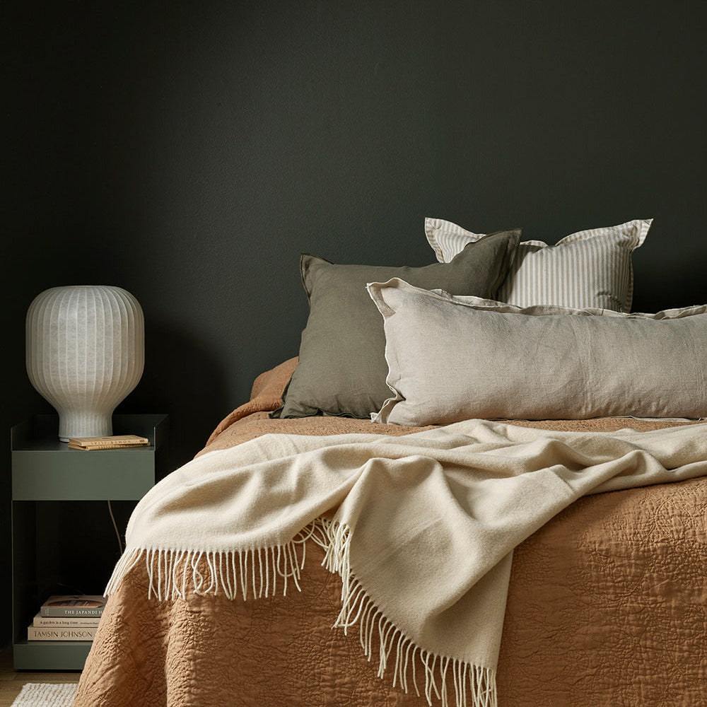 An oyster coloured fringed throw folded across the end of a made bed