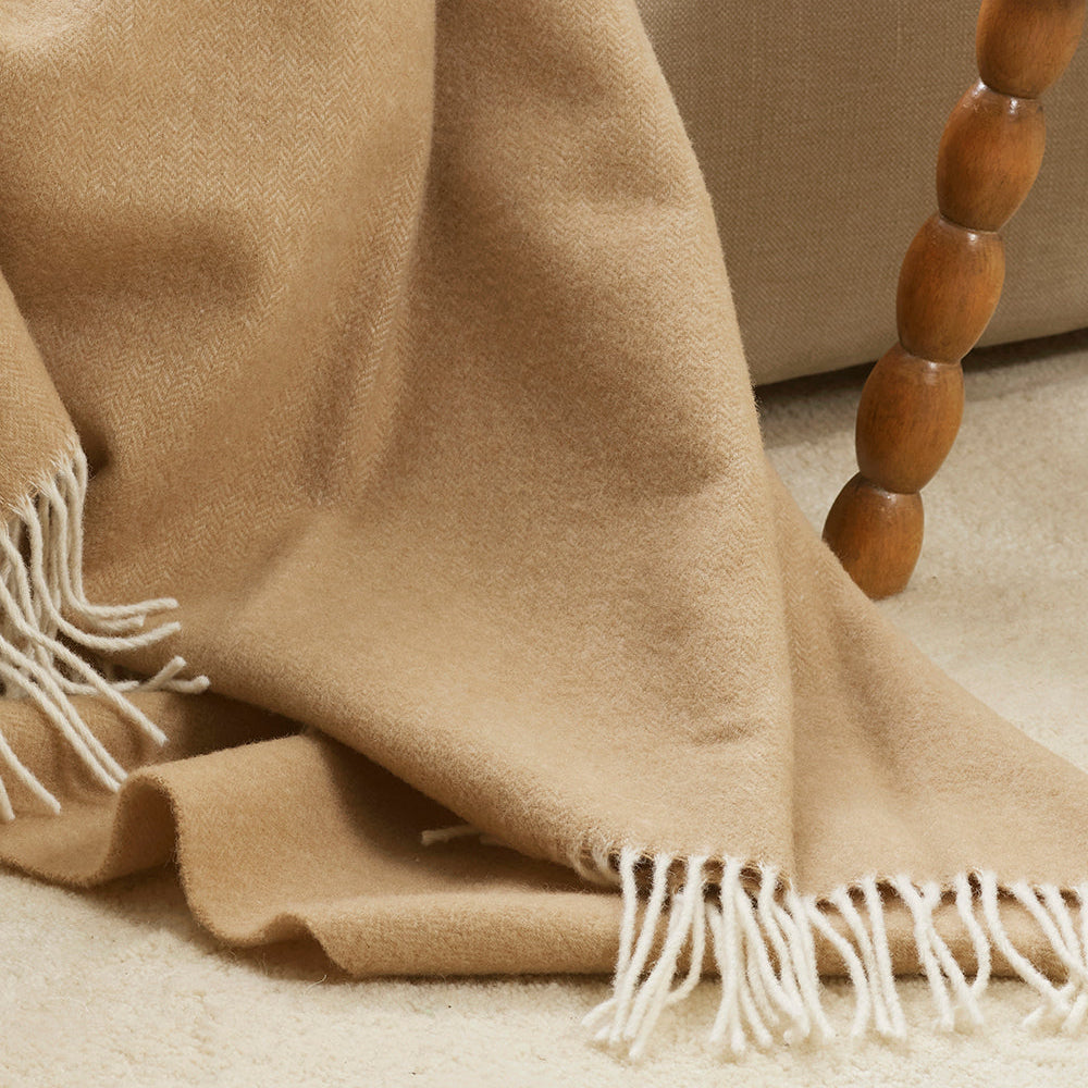Beige blanket with white fringes draped over a wooden chair.