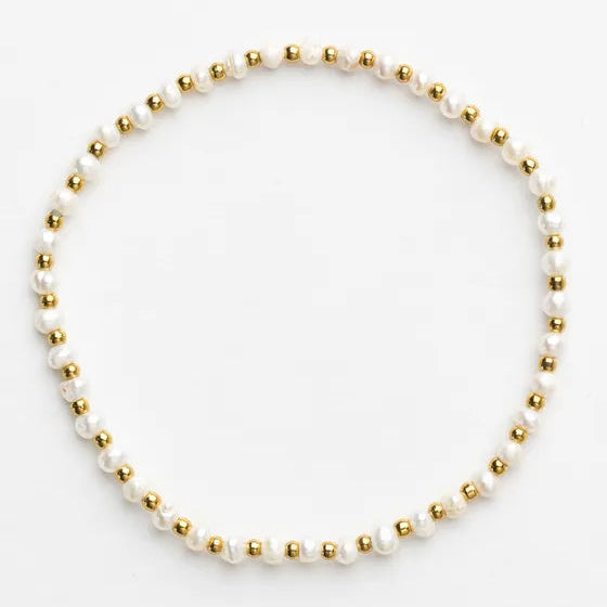 A delicate beaded bracelet featuring white freshwater pearls and small metallic gold beads, arranged in a neat circle on a clean white background.