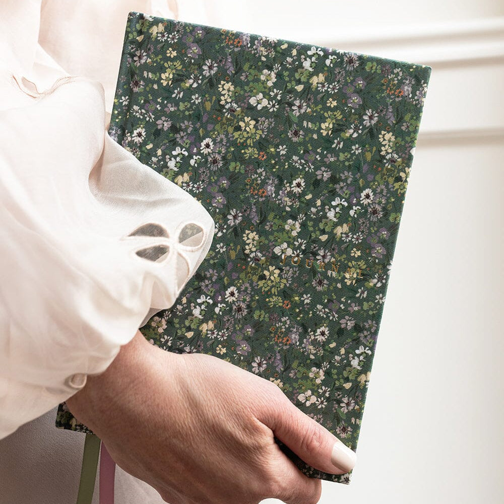 Hand holding a floral-patterned notebook with a white blouse in the background