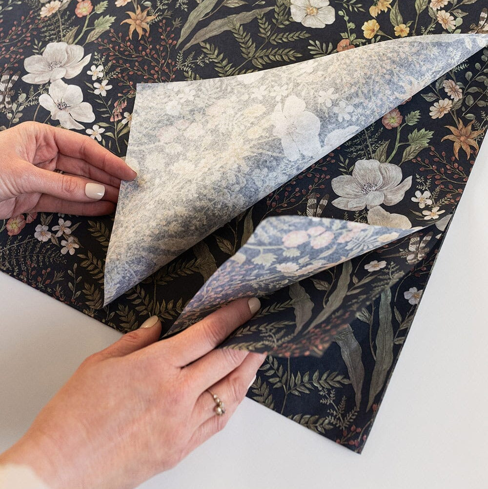 Hands folding floral-patterned paper with a dark background
