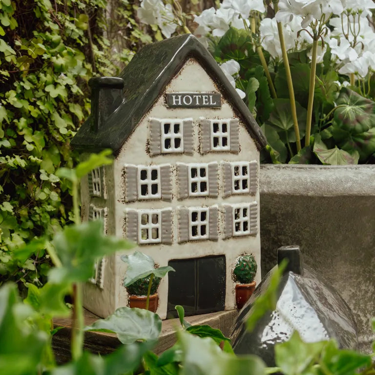 Miniature model of a hotel surrounded by greenery and white flowers. Used for tea light candle.