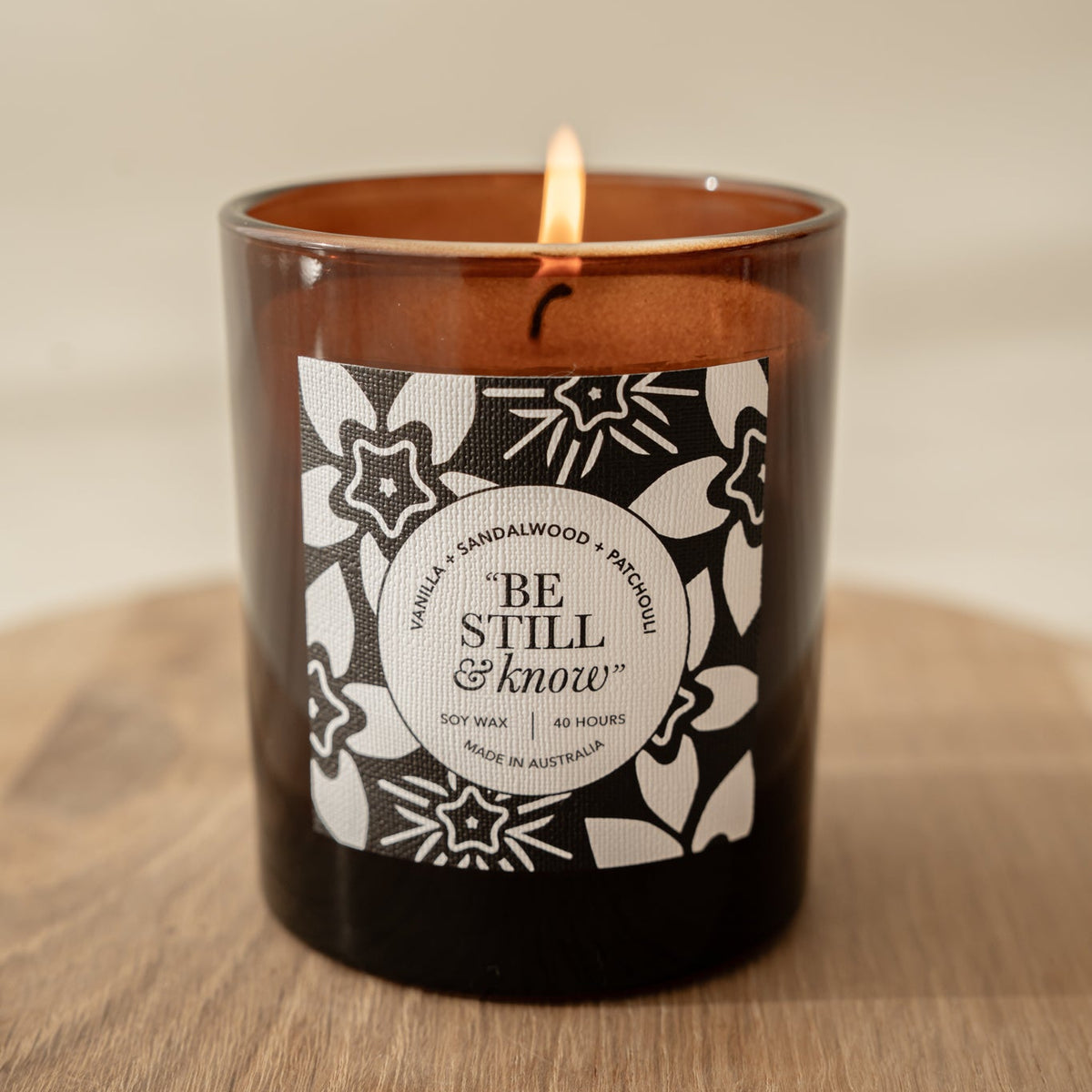 Well Versed Homes Signature Candle with label that says 'be still and know' sitting on a wooden board