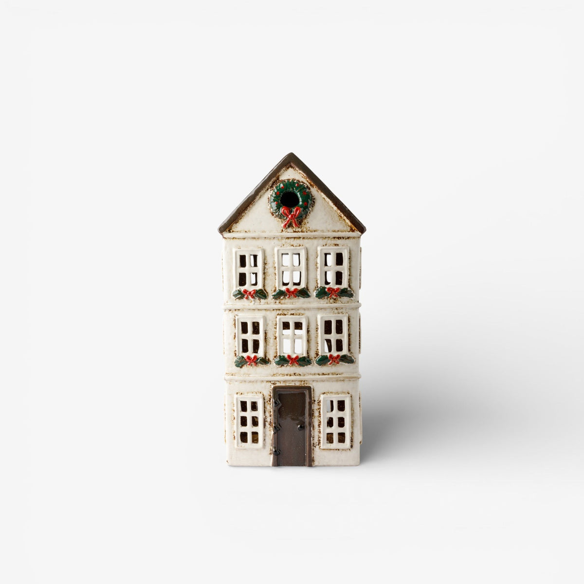 A small decorative house figurine with a white facade, dark brown roof and door, and green holiday wreath details on the roof and windows, shown against a plain white background.