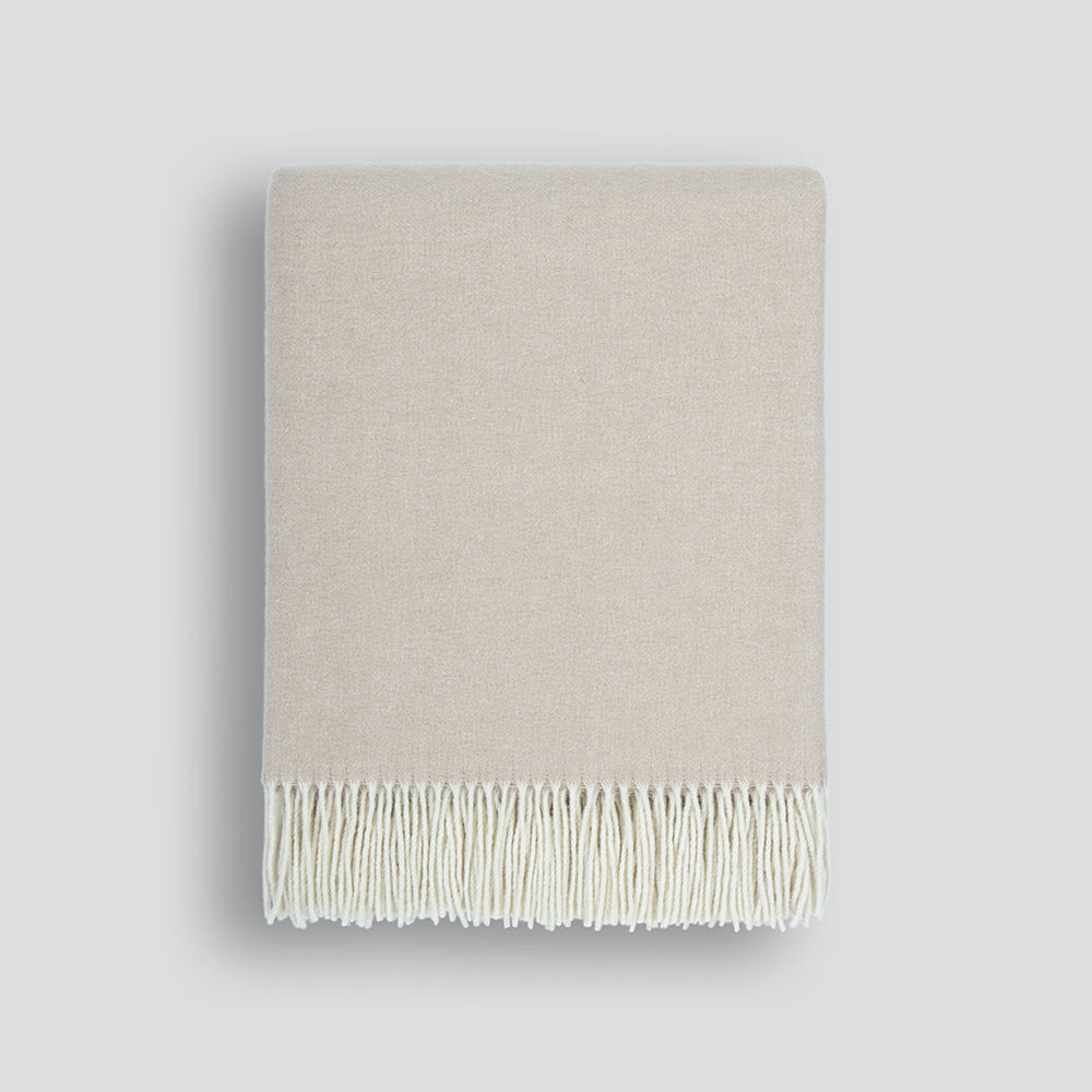Beige blanket with white fringe on a light gray background