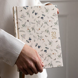Person holding a floral-patterned notebook with '2026' on a neutral background