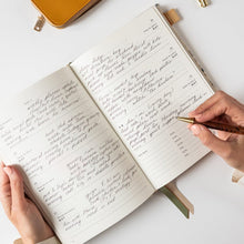 Person writing in a notebook with a pen on a white surface