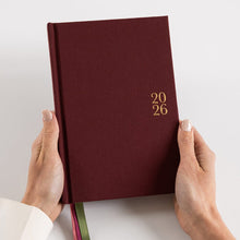 Maroon notebook with '2026' on the cover held by hands against a light background
