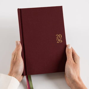 Maroon notebook with '2026' on the cover held by hands against a light background
