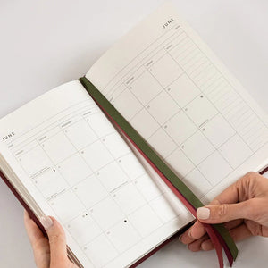 Person holding an open planner with a grid layout on a white background