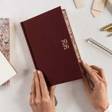 Maroon notebook with '2026' on a white surface with stationery items.