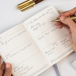 Person writing in a notebook with a gold pen on a white surface