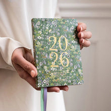 Hand holding a floral notebook with '2026' on a neutral background