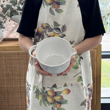 Person holding a white ceramic pitcher with a floral apron