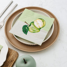 Plates with green apple-themed napkins on a white tablecloth.