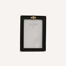 A black rectangular picture frame with a small gold decorative bee accent at the top centre.