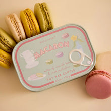 A rectangular macaron-themed soy wax candle tin with a white pull tab, styled on a beige background with colorful macaron cookies.