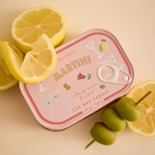 A pink candle in candle with Martini fragrance, styled including a lemon and olives on a warm beige background.