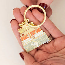 Gold keychain with decorative elements held in a hand against a white background