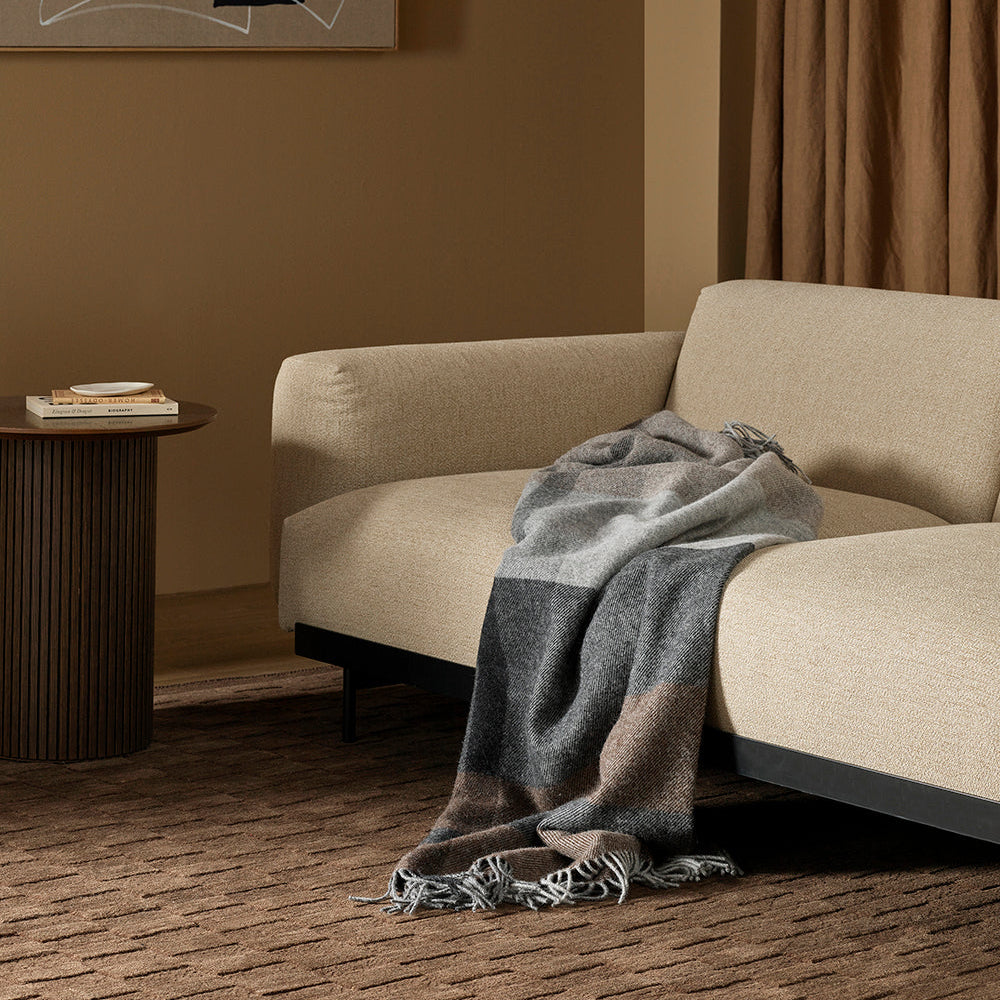 Beige sofa with a gray blanket in a room with abstract art and brown curtains.