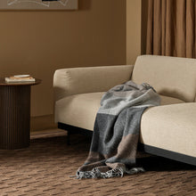 Beige sofa with a gray blanket in a room with abstract art and brown curtains.