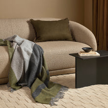 Beige sofa with a green and gray blanket and brown pillow in a living room setting.