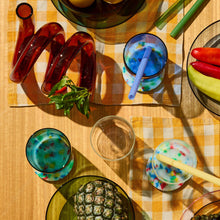 Colorful drinks in glasses on a checkered tablecloth with lemons, pineapple, and other items.