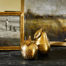 Gold apple and pear on black table with photo frame and artwork in background