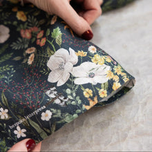 Person holding a piece of floral fabric with white flowers on a dark background.