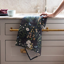 Floral towel hanging on a kitchen cabinet handle with a sink and fruit in the background