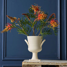 Decorative plant arrangement in a white vase against a dark blue wall.