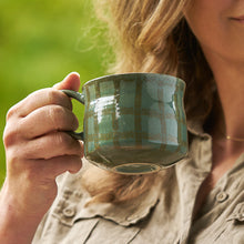Person holding a green mug outdoors with a blurred green background