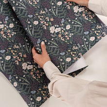 Person handling a roll of floral-patterned gift wrapping paper on a white surface