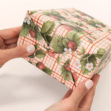 Hand holding a small box with strawberry patterned gift wrap on a white background