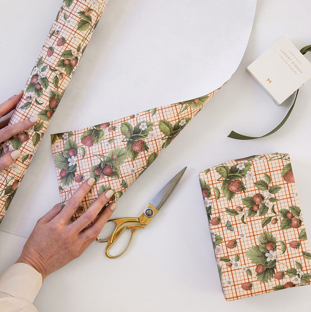Person cutting a piece of strawberry-patterned paper with scissors on a white surface