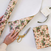 Person cutting a piece of strawberry-patterned paper with scissors on a white surface