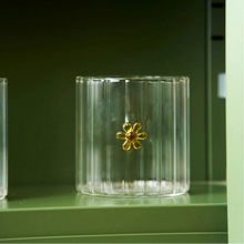 Clear glass with a gold flower decoration on a green shelf.