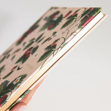 Hand holding recipe journal with floral pattern on a light background