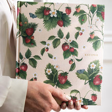 Hand holding a recipe book with strawberry and leaf pattern