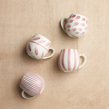 Set of four ceramic cups with different patterns on a beige surface