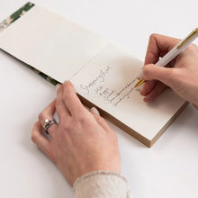 Person writing in a notebook with a pen on a white surface
