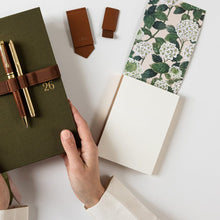 Green notebook with pen, brown wallet, and floral-patterned box on a white surface