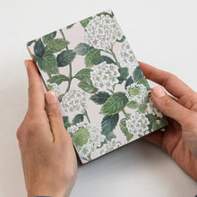 Hand holding a small notebook with floral design on a light background