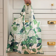 Person holding a floral-patterned reusable bag in front of a kitchen cabinet.