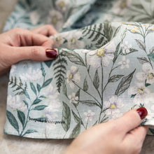 Floral patterned fabric held by hands with red nail polish on a neutral background