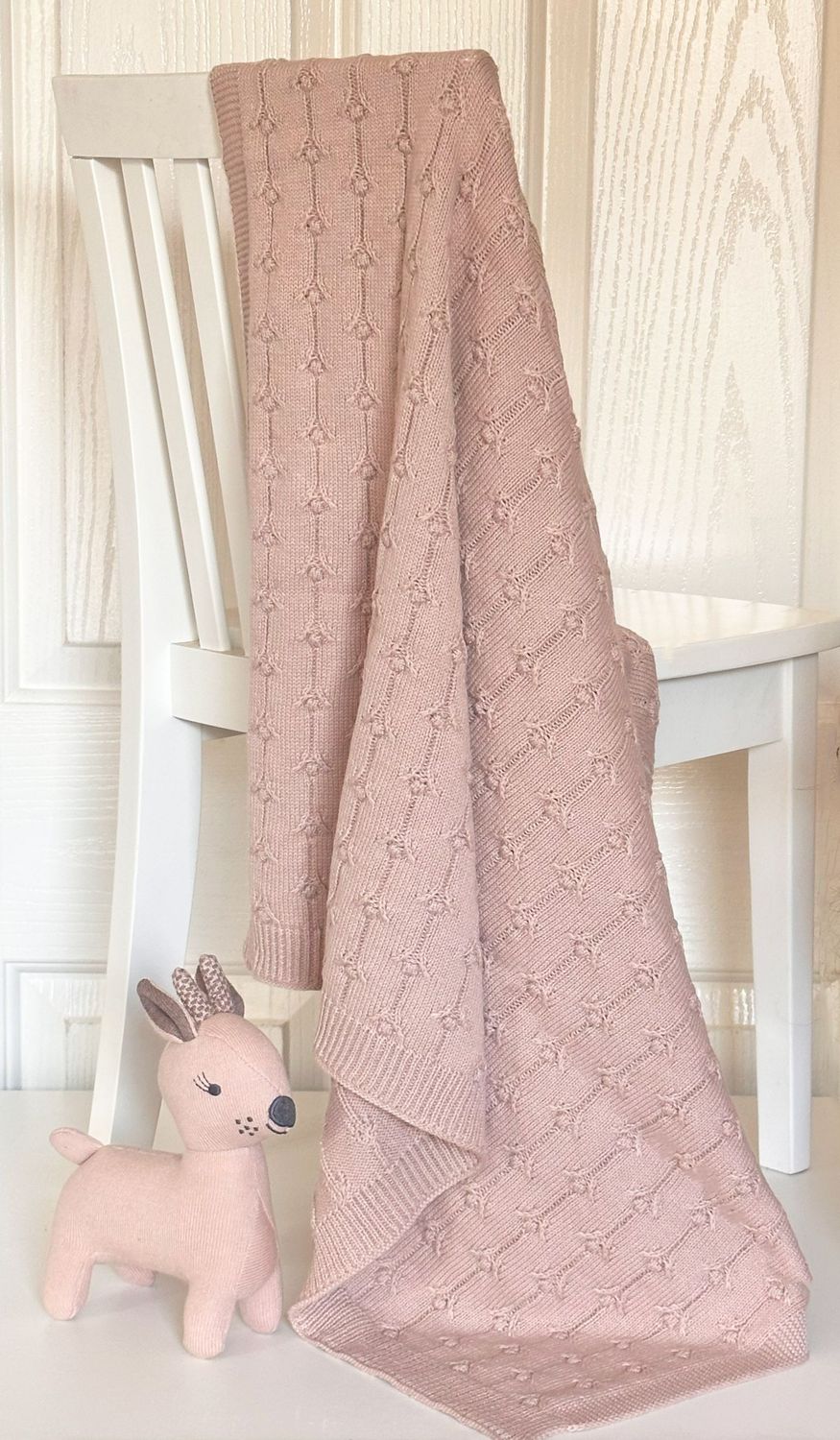 Pink knitted baby blanket hanging on white chair