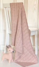 Pink knitted baby blanket hanging on white chair