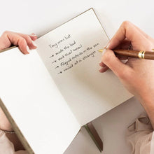 Person writing in a notebook with a pen on a white surface